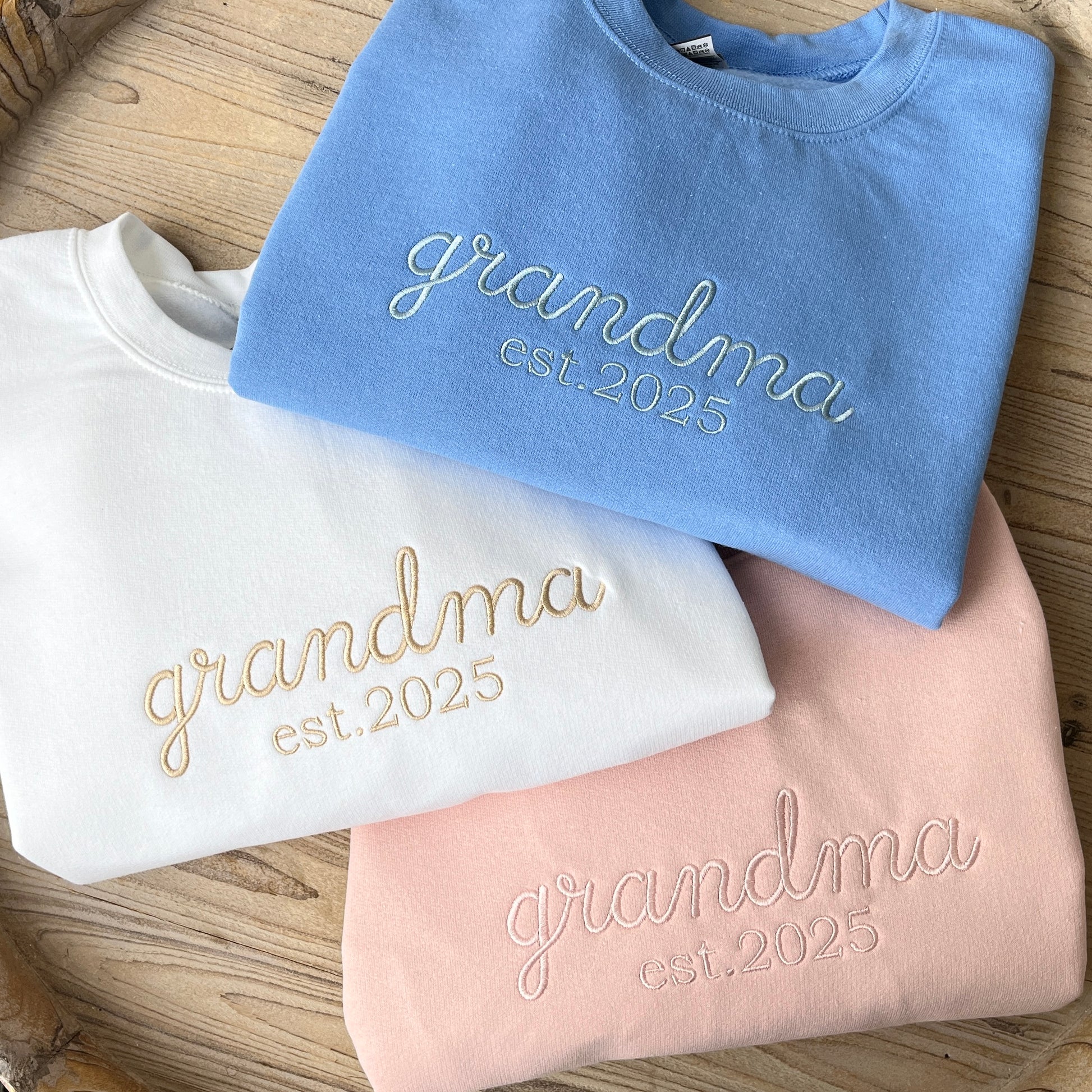 group of 3 crewneck sweatshirts: Carolina blue with grandma est. 2025 embroidered in powder blue, white with grandma est. 2025 embroidered in camel thread, blush with grandma est. 2025 embroidered in powder pink thread