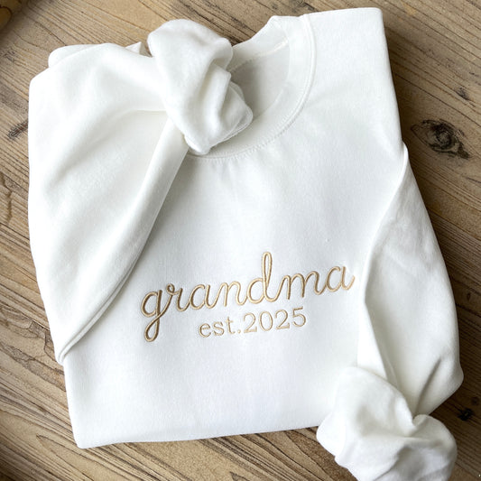 closeup of white crewneck sweatshirt with custom embroidered grandma est. 2025 design in camel thread