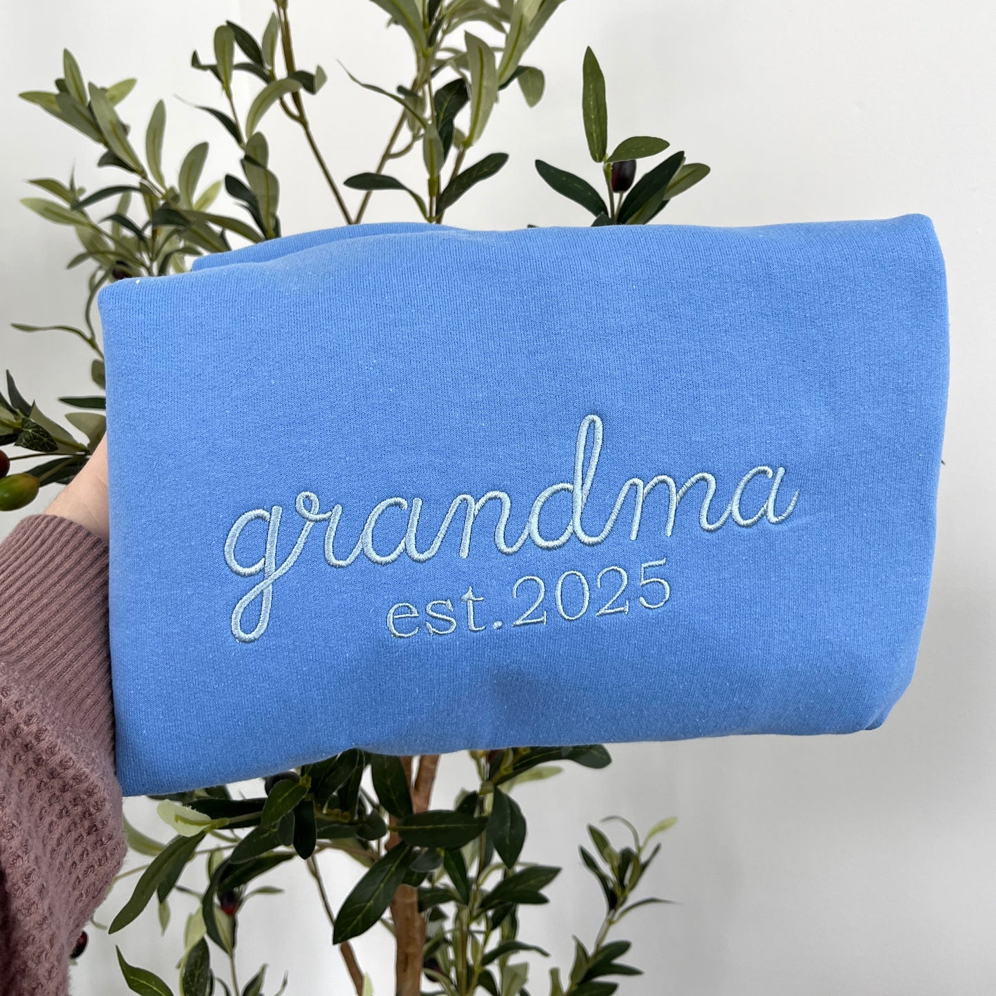 closeup of carolina blue crewneck sweatshirt with custom embroidered grandma est. 2025 design in powder blue thread