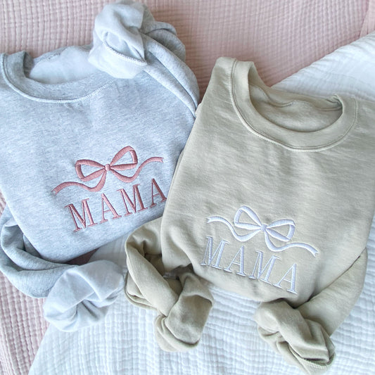 flat lay photos of an ash crewneck sweatshirt and a sand crewneck sweatshirt with embroidered bow and mama design in mauve and white thread