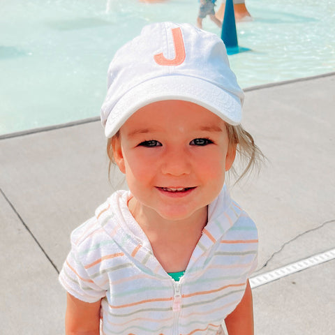 toddler wearing a white baseball cap featuring a single embroidered large initial 