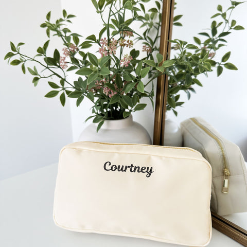 creme accessory pouch with a custom embroidered name in a script font along the top of the bag. mini embroidery 