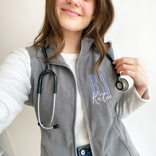 selfie of a young woman wearing a grey flecce vest with personalized RN embroidered design