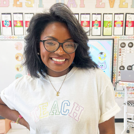 teacher wearing a pastel rainbow open block teach embroidered t-shirt