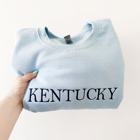 light blue crewneck sweatshirt with embroidered Kentucky in navy thread