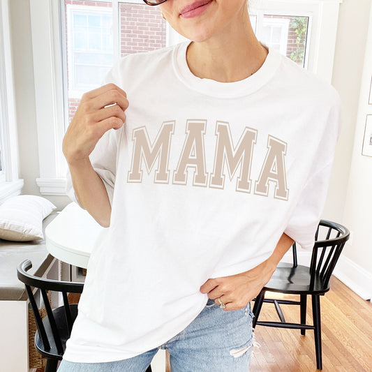 woman wearing an oversized white comfort colors t-shirt with a light mocha brown varsity style mama print across the chest in large letters
