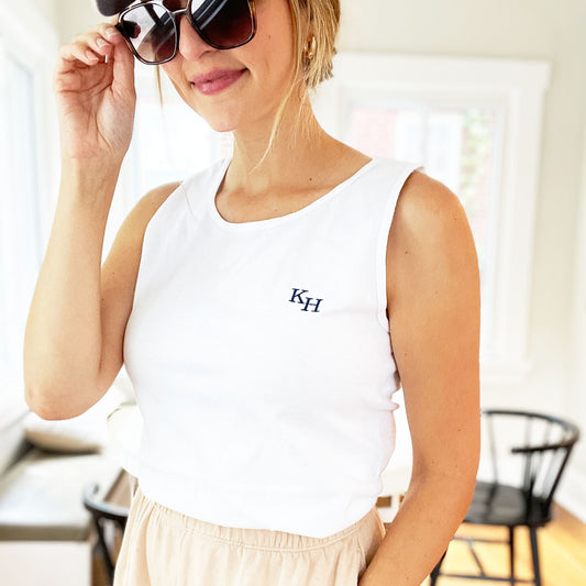 woman wearing a baseball hat, sunglasses, shorts, and a white comfort colors tank top with a personalized staggered embroidered monogram
