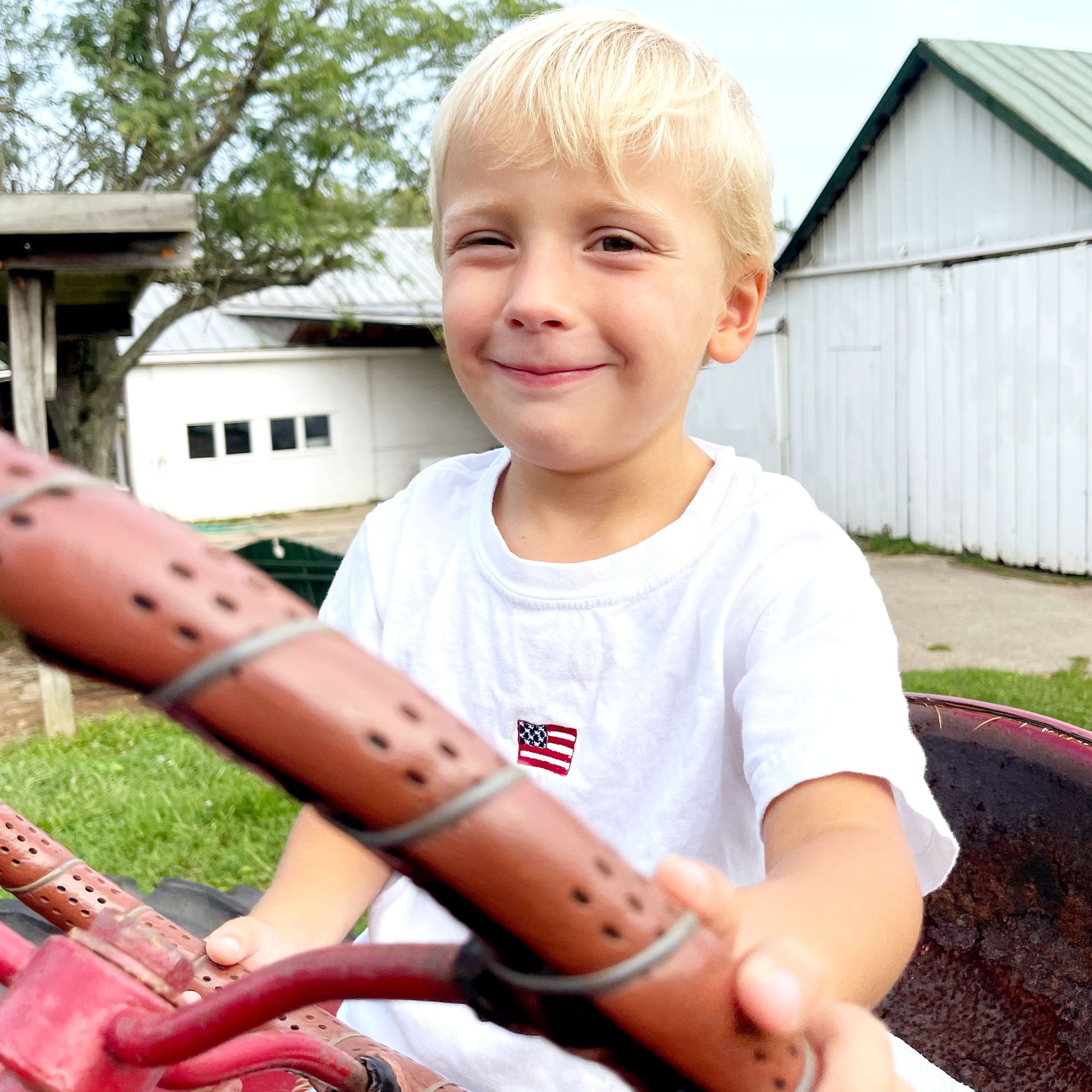 little boy on a tractor wearing a white mini flag embroidered tshirt