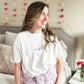 young woman wearing a white tee with two tones purple xoxo embroidered small on the center chest