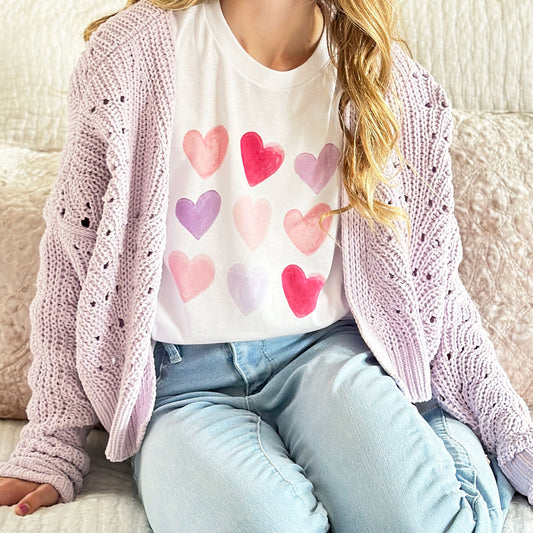 young girl wearing a white t-shirt with a valentine's watercolor heart print and a purple cardigan