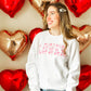 young woman in front of heart balloons modeling a white crewneck sweatshirt with lover printed design filled with valentine's hearts