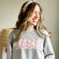 toung woman styling an athletic heather crewneck sweatshirt with MAMA printed in a pink and purple hearts design 