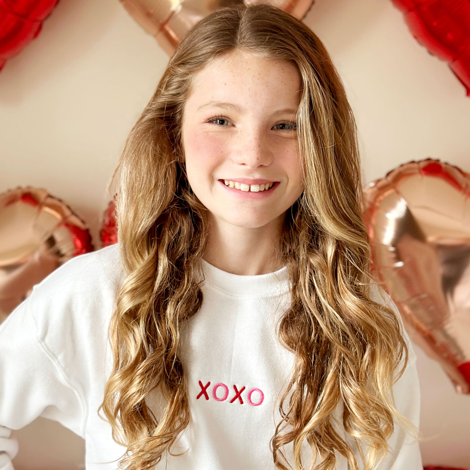 young girl wearing a white sweatshirt with an xoxo embroidered valentine's design