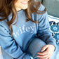 Young woman wearing a slate blue crewneck sweatshirt with wifey embroidered in a floral lettering