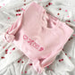 light pink crewneck sweatshirt with a heart, cupids bow and arroe, heart envelope, and a rose embroidered in pink across the chest