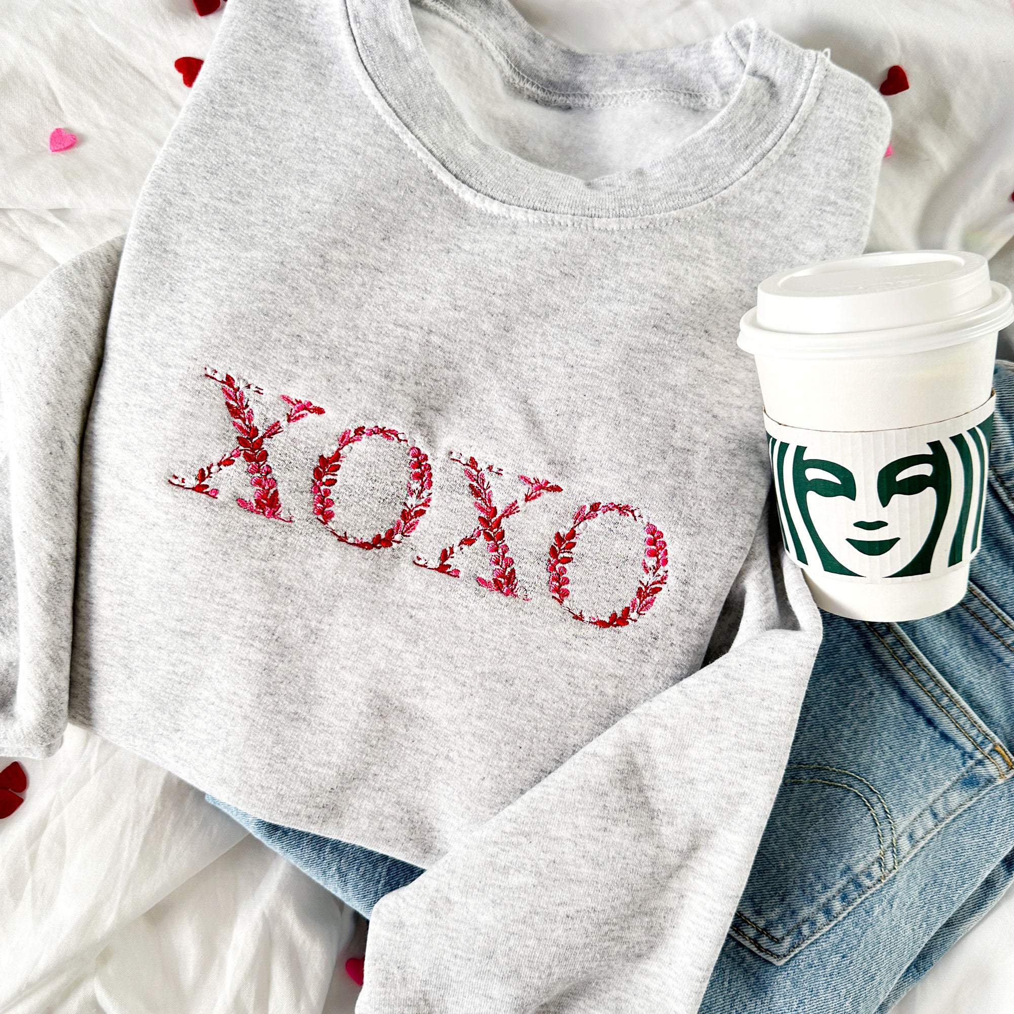 Gray sweatshirt with 'XOXO' text, Starbucks cup, and denim jacket on a white background