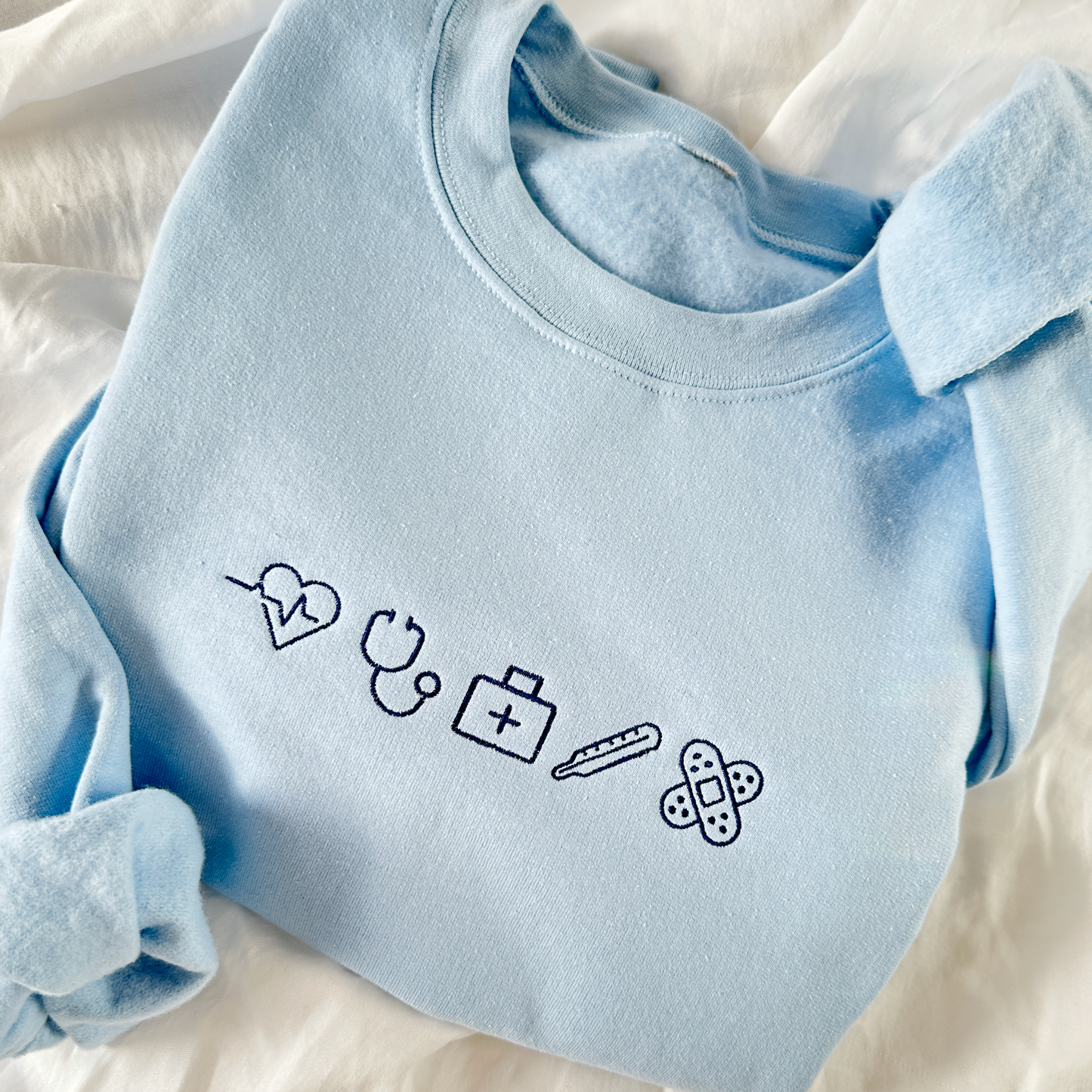 light blue crewneck sweatshirt with navy embroidered  nurse icons across the chest.