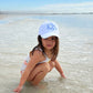 young girl playing on a beach with a white baseball cap with embroidered monogram in periwinkle thread