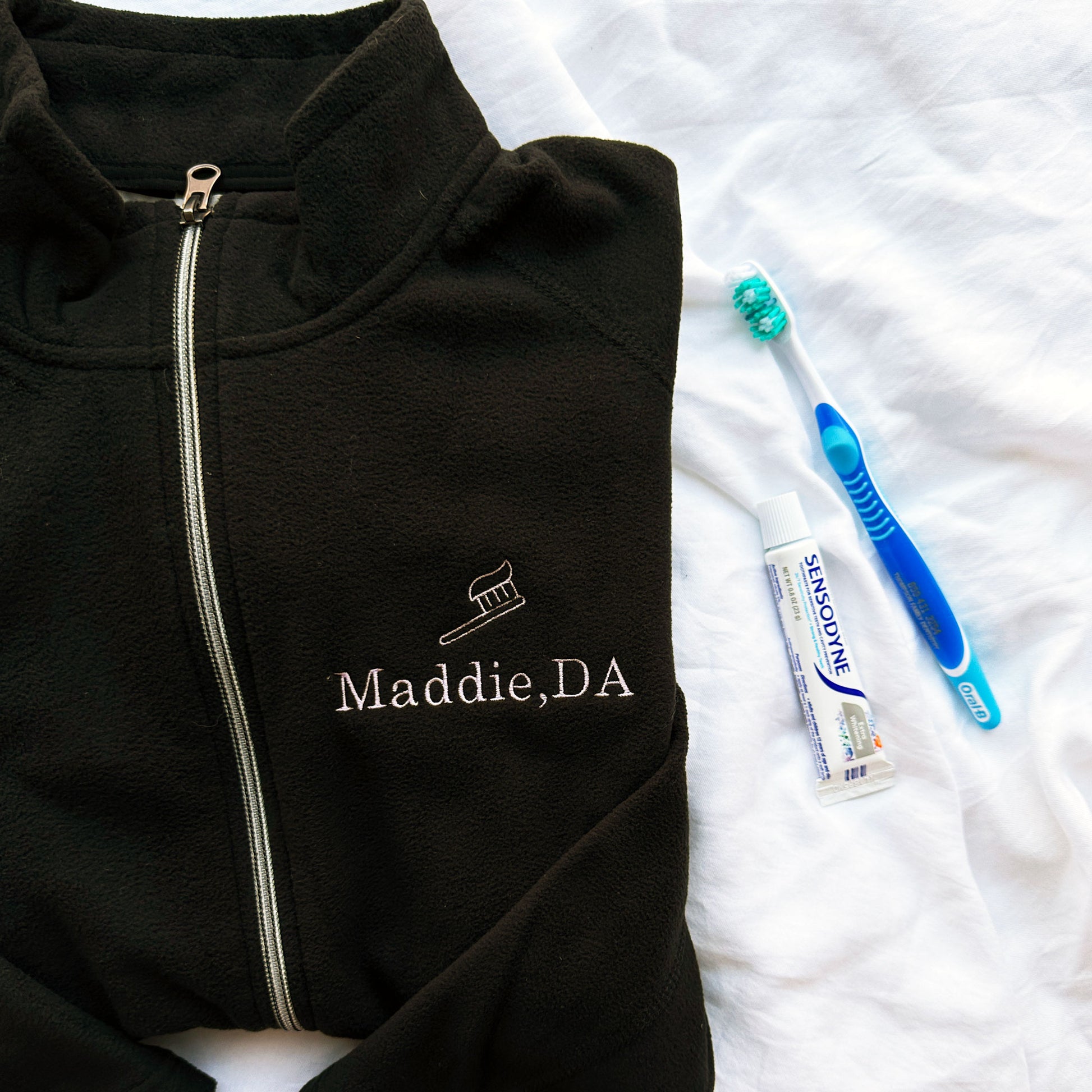 full zip fleece black jacket with mini embroidered toothbrush outline and name Maddie DA in lilac thread on the left chest