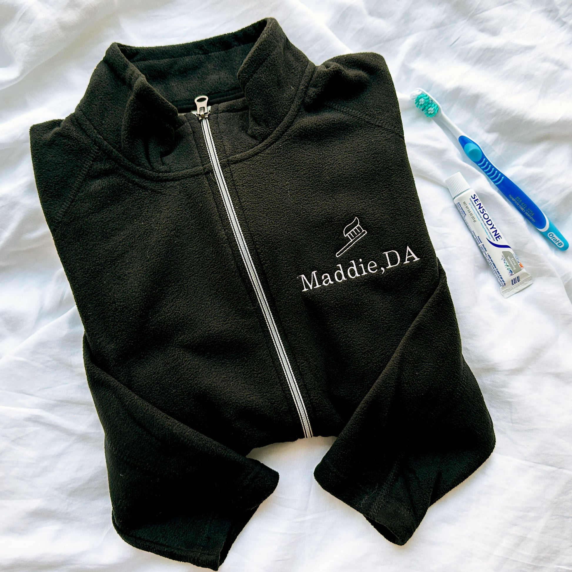 full zip fleece black jacket with mini embroidered toothbrush outline and name Maddie DA in lilac thread on the left chest