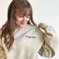 woman wearing a sand crewneck sweatshirt with a custom large heart embroidered stethoscope with her name embroidered through the center in a script font