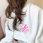 Woman wrapped in a white blanket with SME monogram embroidered on the corner in pink thread