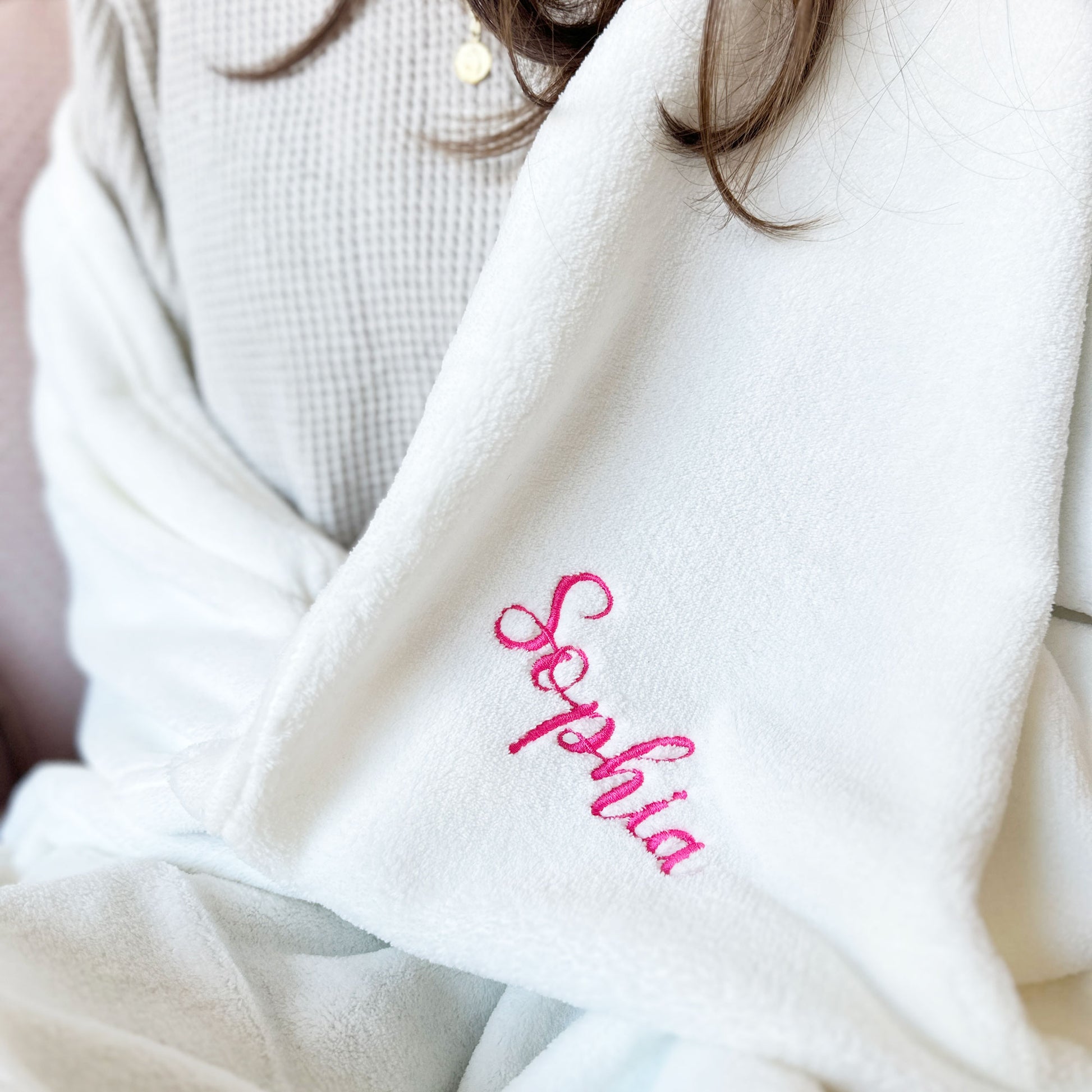 close up of woman wrapped in a white blanket with sophia embroidered on the corner in pink thread.
