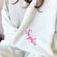 close up of woman wrapped in a white blanket with sophia embroidered on the corner in pink thread.