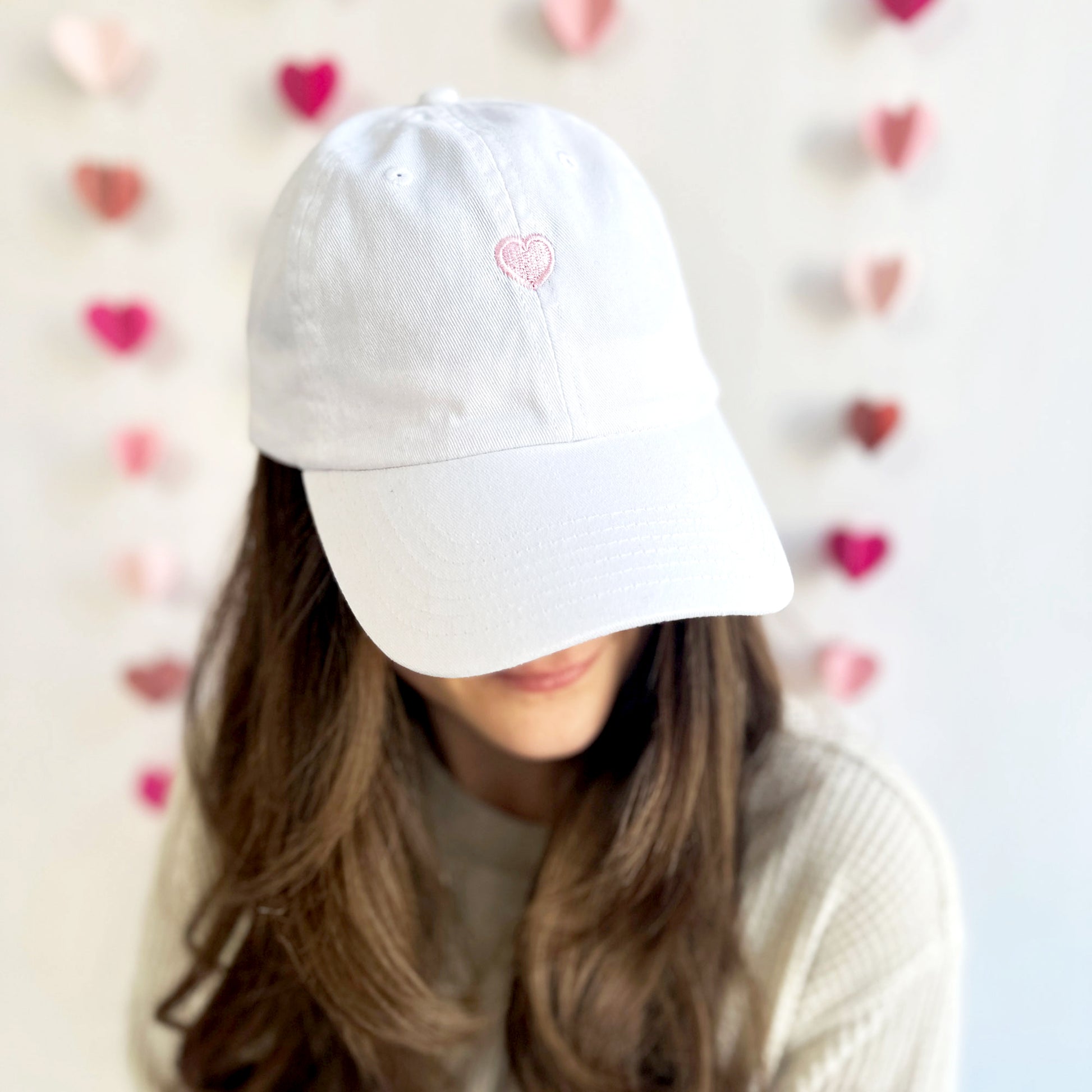 young woman wearing a white baseball cap with baby pink embroidered heart