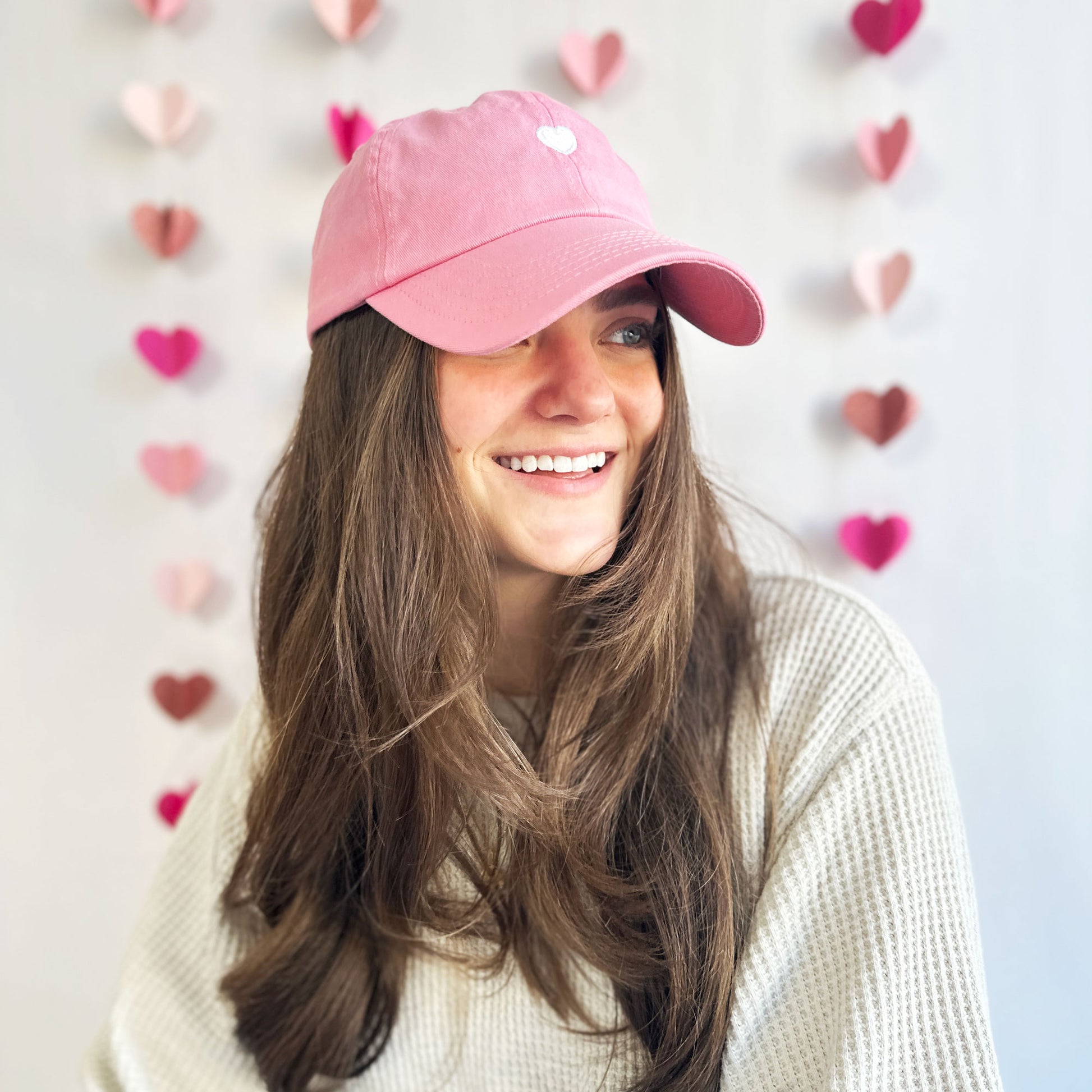 young woman wearing a pink baseball cap with mini white embroidered heart