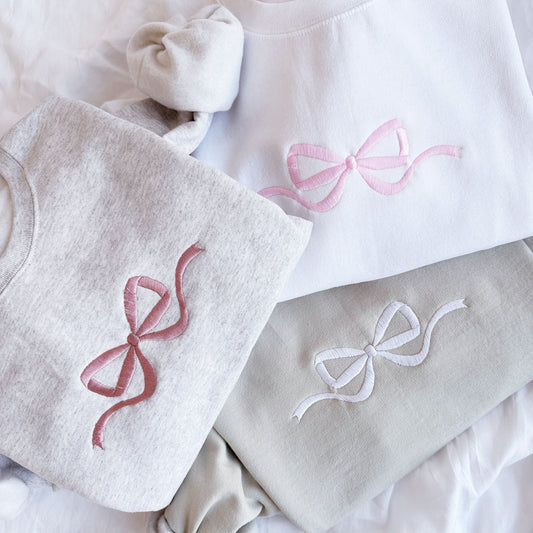 Flat lay of three sweatshirts with different colored embroidered bow design.