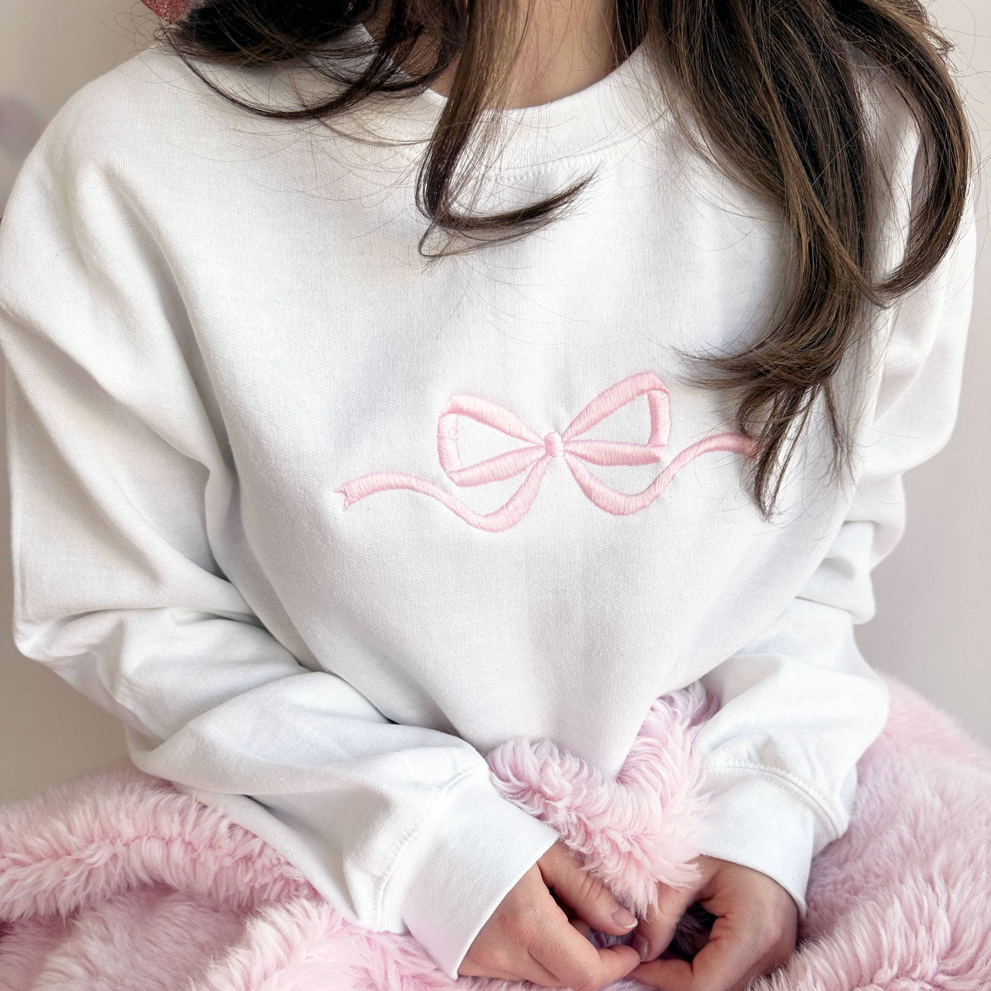 Close up of woman wearing a white crewneck sweatshirt with a baby pink embroidered bow