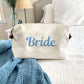 White addison dopp kit with script bride embroidered in baby blue thread on the center of the bag styled on a bed