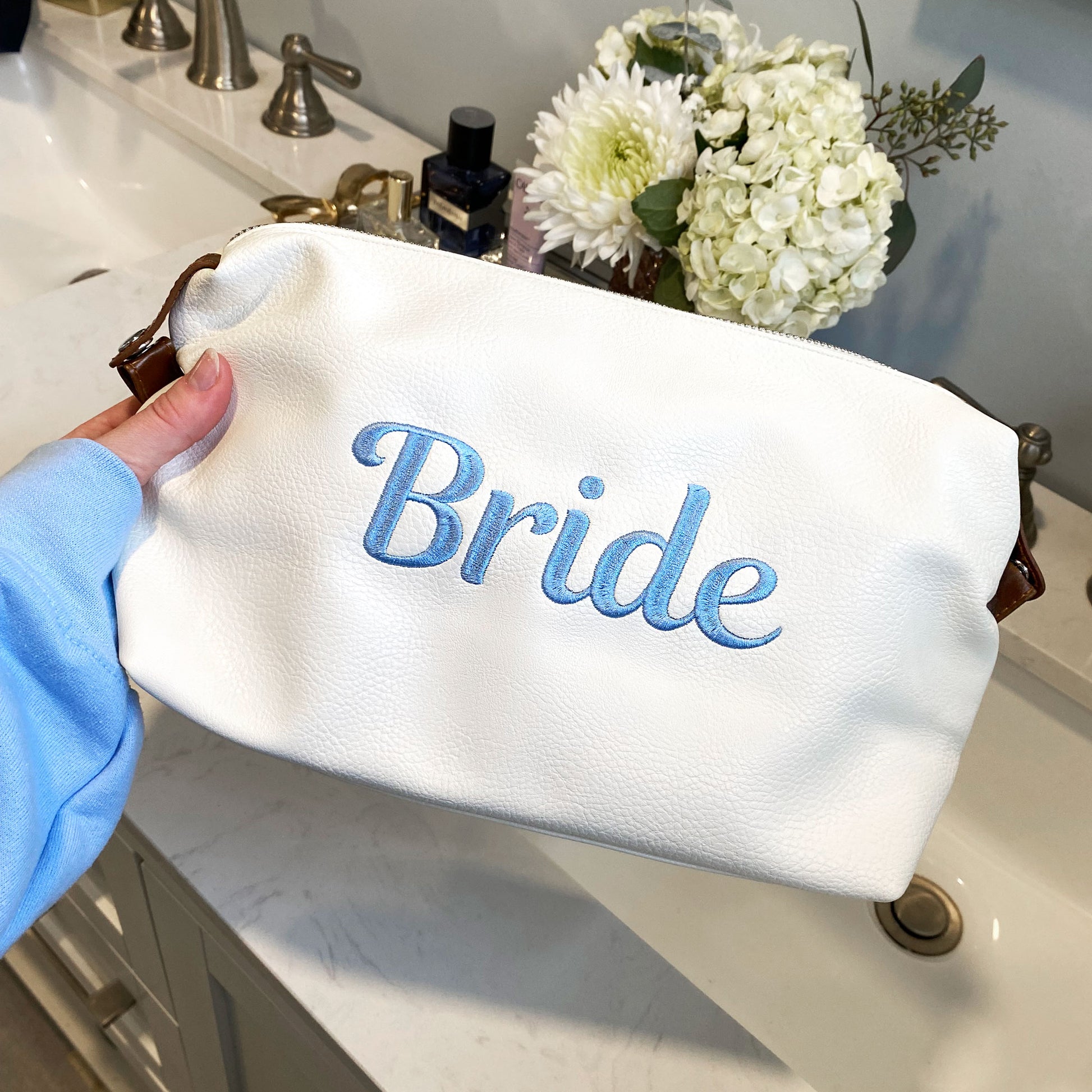 White addison dopp kit with script bride embroidered in baby blue thread on the center of the bag