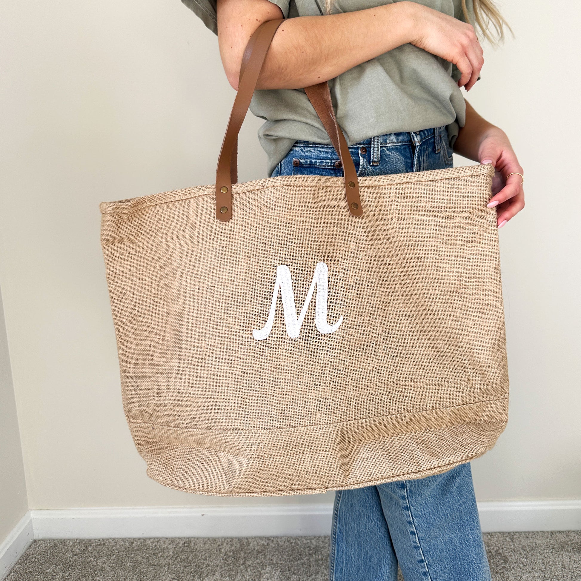 woman with a natural jute tote bag on the crook of her arm with a personalized embroidered initial