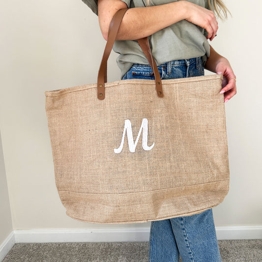 woman with a natural jute tote bag on the crook of her arm with a personalized embroidered initial