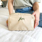 woman holding a small cosmetic pouch in taupe with mini jhm initials embroidered in olive thread