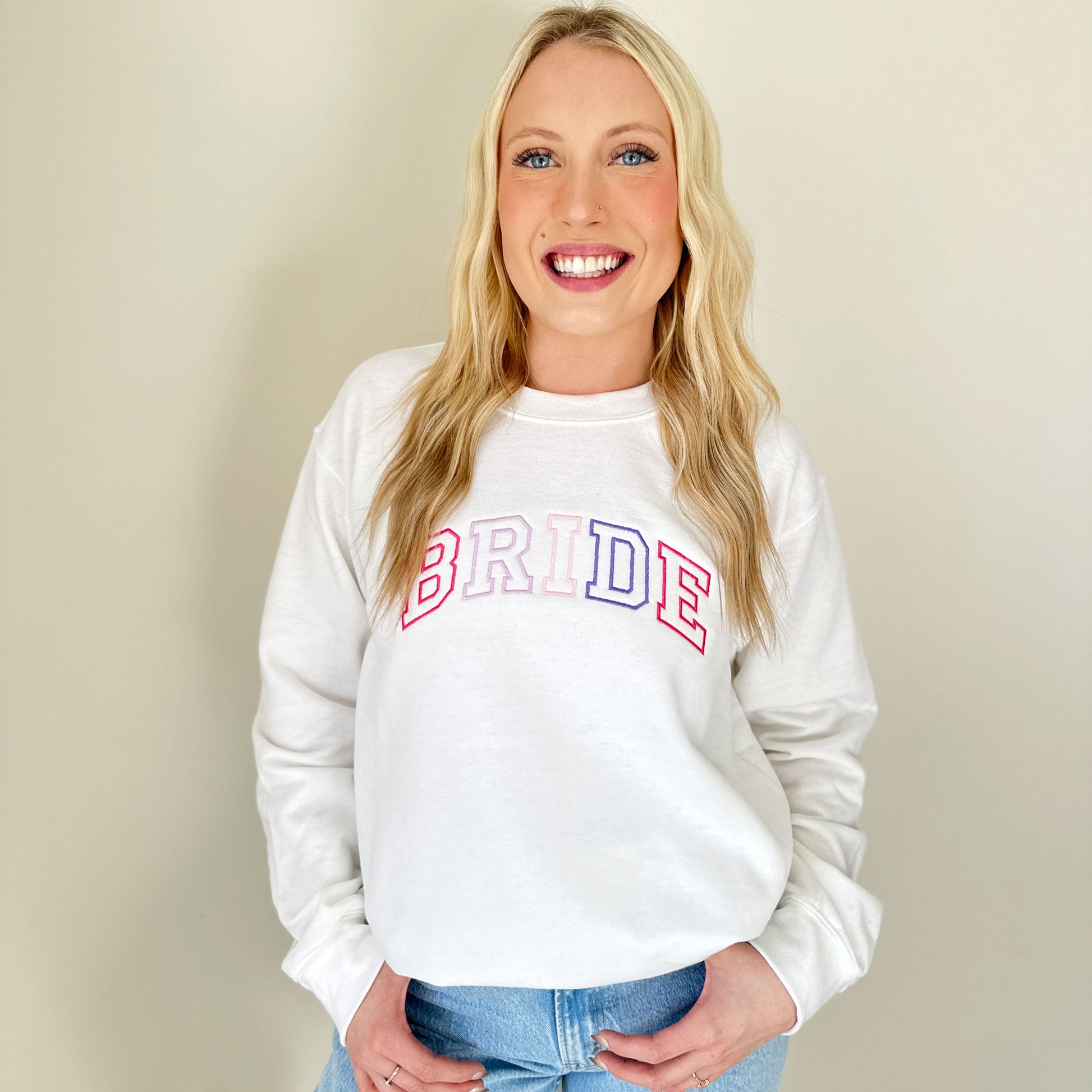 woman wearing a white pullover sweatshirt with purple and pink embroidered BRIDE design across the chest