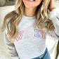 woman wearing a light gray sweatshirt with wifey embroidered across the chest in a pink and purple thread combination