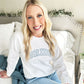 bride sitting on her bed, wearing a white crewneck sweatshirt with BRIDE embroidered in an athletic block outlined font on the front