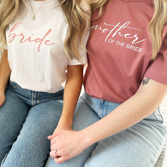 2 ladies waring bella and canvas crewneck tees one in white with bride printed and one in mauve with mother of the bride printed across the chest