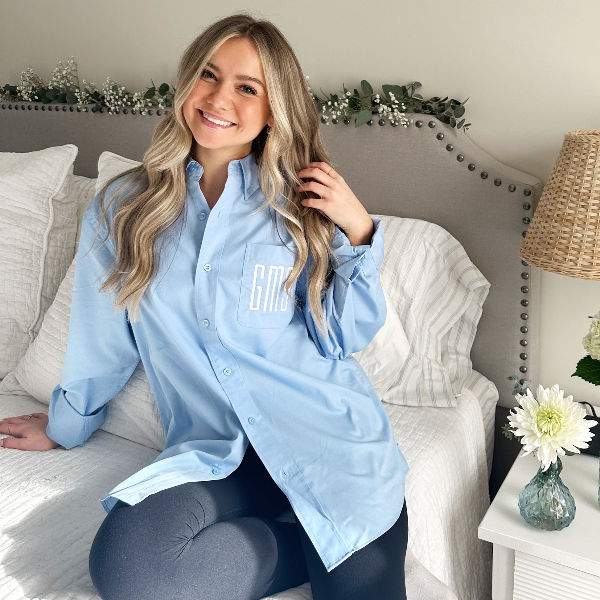 young woman wearing a light blue button up with monogram embroidery on the pocket in white thread