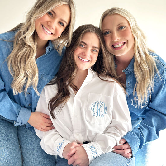 bride and 2 bridesmaids wearing burron down monogram shirts, the bride is wearing  a white button down with  monogram and cuff embroidery in baby blue thread