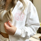 close up of a while full zip hooded sweatshirt with monogram embroidery in baby pink 
