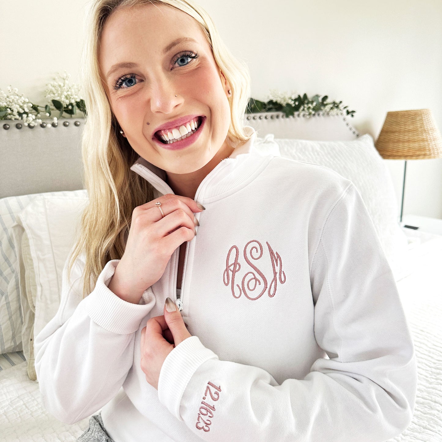 young woman wearing a white quarterzip sweatshirt with monogram and cuff embroidery in mauve thread 