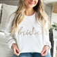 Close up of a woman wearing a white crewnecksweatshirt with script bride embroidered in camel thread