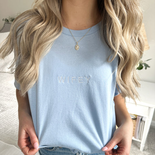close up of a minimal Wifey text embroidered in white on a baby blue crewneck t-shirt