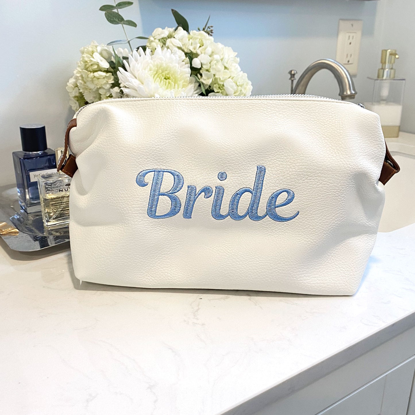 White addison dopp kit with script bride embroidered in baby blue thread on the center of the bag styled on a bathrom counter