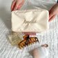 cream cosmetic pouch with embroidered name and beauty products laying around 