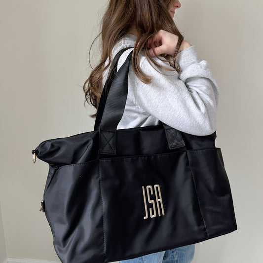 woman with a black nylon duffle on her shoulder, bag featuring a custom embroidered monogram
